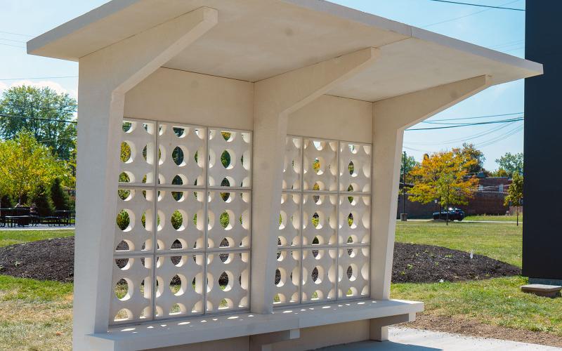 "La Distancia/ The Distance" artistic concrete bus Shelter on concrete slab, mulch in background