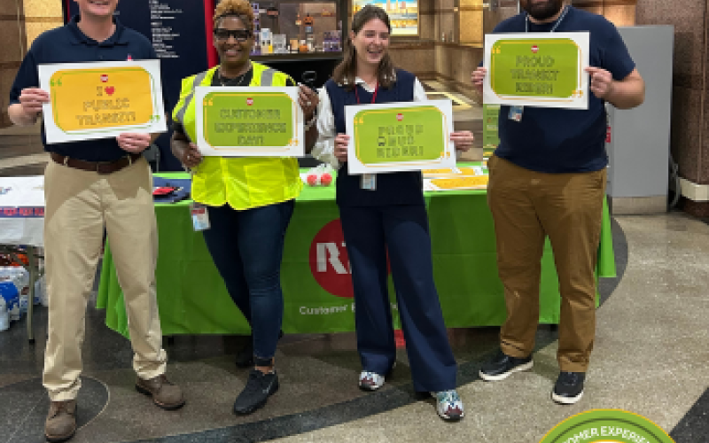 GCRTA Customer Experience Team standing in front of a table, holding grean and yellow signs