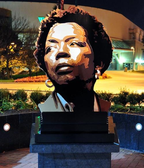 8 abstract sheets of various colored metal stand straight up out of a solid granite base. At most angles, this piece looks like a random arrangement of random shapes. However, when viewed directly head-on from either side, a portrait of Stephanie Tubbs Jones appears; black and white on one side and in color on the other.